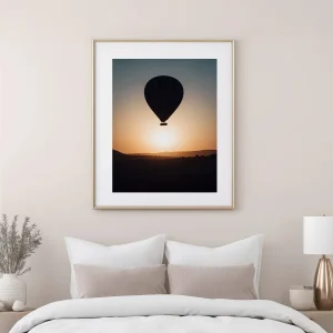 Cadre bois clair montgolfière Cappadoce au-dessus d'un lit dans une chambre aux tons beiges.
