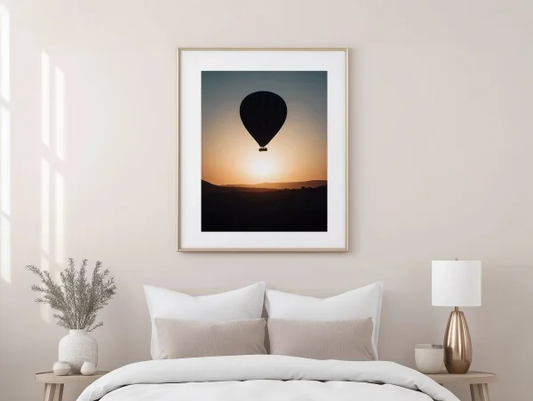 Cadre bois clair montgolfière Cappadoce au-dessus d'un lit dans une chambre aux tons beiges.