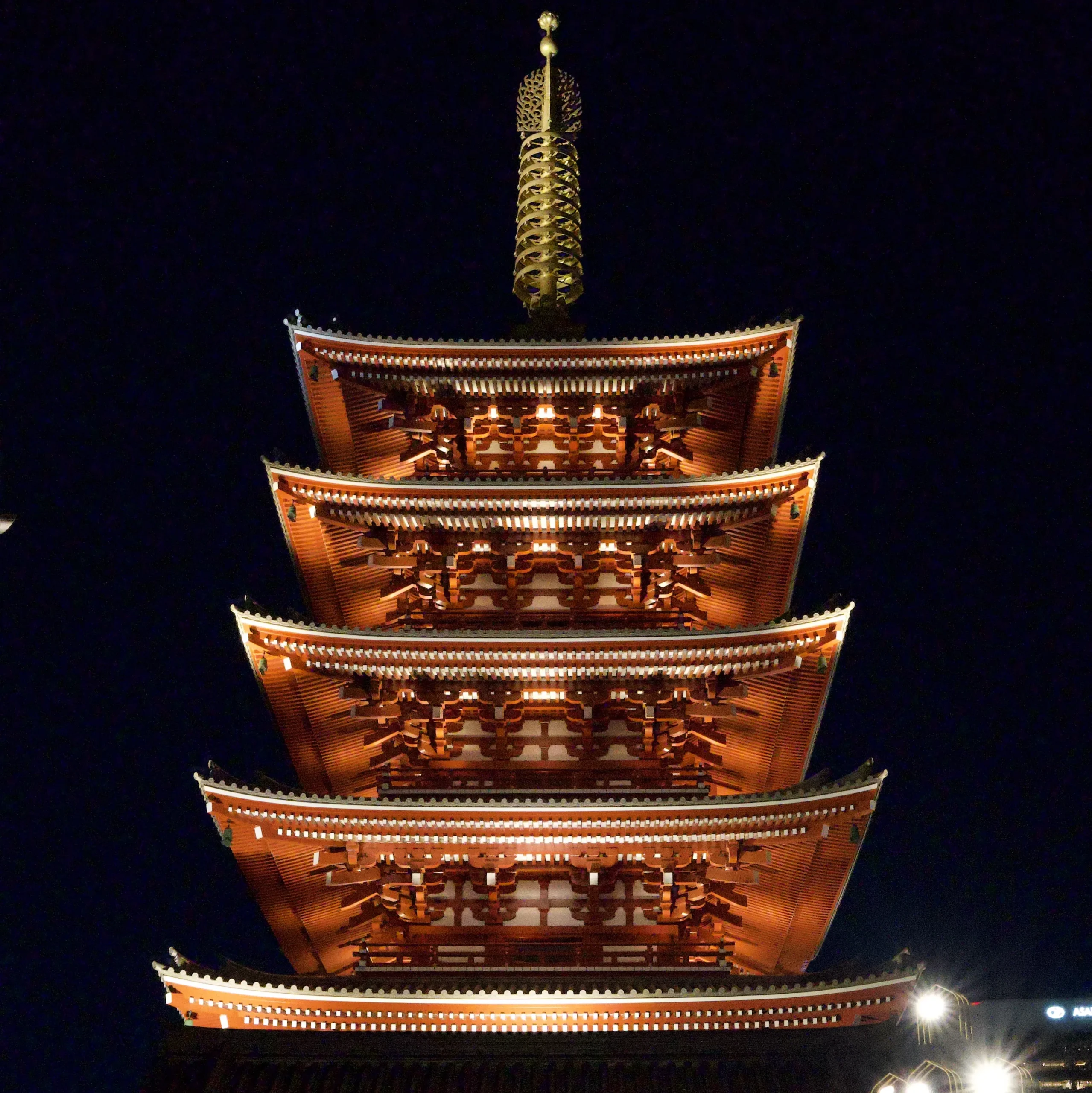 Une pagode japonaise traditionnelle à cinq étages, peinte en rouge et or, brillamment illuminée la nuit contre un ciel noir Senso-JI