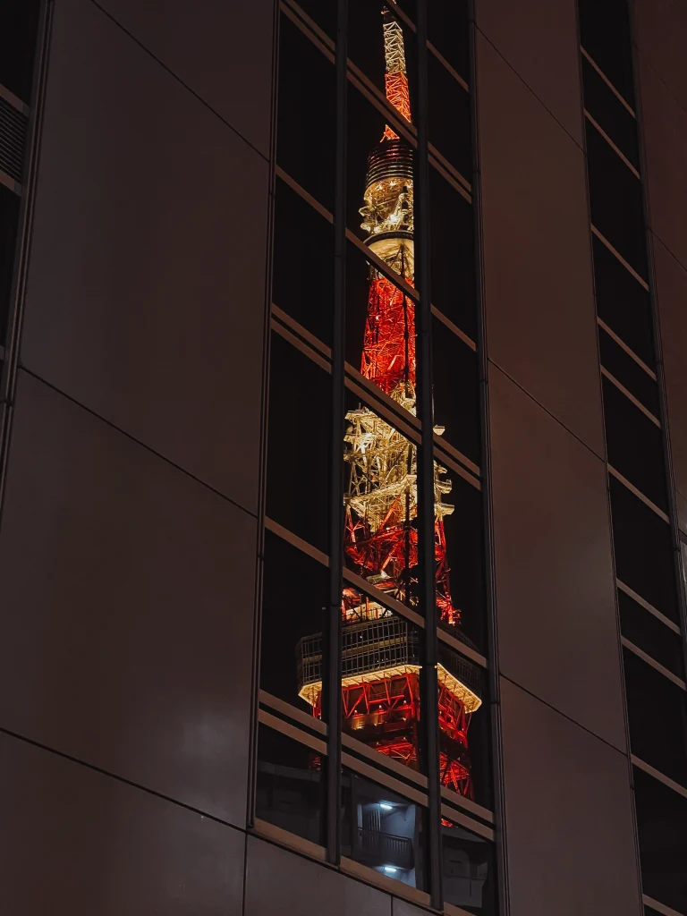 Tirage d'art nocturne et urbain de la Tokyo Tower illuminée en rouge, se reflétant dans les vitres d'un gratte-ciel moderne au Japon.